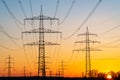 Electricity pylons and electric power transmission lines against vibrant orange sky at sunset. High Voltage towers provide power. Royalty Free Stock Photo