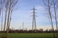 Electricity pylons and over head cables in the middle of a field framed by bare trees in the italian countryside