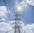 Electricity transmission lines and pylon silhouetted against blue sky and cloud,high voltage tower , light and flare effect added Royalty Free Stock Photo