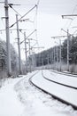 Electrified railway line with poles for wires at winter season, an empty road Royalty Free Stock Photo