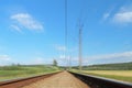 An electrified railway track among green meadows and wheat fields. Mound of coarse gravel with rails and sleepers for transporting Royalty Free Stock Photo