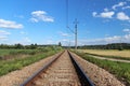 An electrified railway track among green meadows and wheat fields. A sunny day with a clear blue sky with clouds. Technology of tr Royalty Free Stock Photo