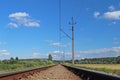 An electrified railway track among green meadows and wheat fields. A sunny day with a clear blue sky with clouds. Technology of tr Royalty Free Stock Photo