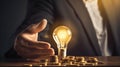 Electrifying Perspective: Light Bulb Held by Hand Over Coins on Desk