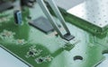 Electronic component in tweezers above a PCB