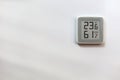 Electronic digital thermometer on white wall showing temperature, humidity level