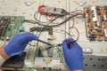 Electronic engineer repairs large TV in service center. Gloved hands measure current resistance with test leads of multimeter.