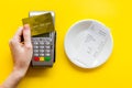 Electronic payments in restaurant. Hand bring bank card to terminal near bill on yellow background top view Royalty Free Stock Photo