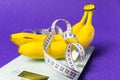 On the electronic scale are two bananas and a measuring tape on a purple background Royalty Free Stock Photo