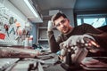 Electronic technician in goggles, leaning on a desk in a repair shop, looking at a camera with a thoughtful look