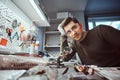 Electronic technician in goggles, leaning on a desk in a repair shop, looking at a camera with a thoughtful look