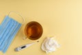 Electronic thermometer, cup of tea, mask and green pills on yellow background. Royalty Free Stock Photo