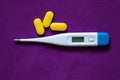 electronic thermometer lies next to yellow pills on an isolated background, medicine and pharmacy, health and treatment Royalty Free Stock Photo