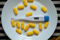 an electronic thermometer lies next to yellow pills on a plate on the table in the kitchen, medicine and pharmacy Royalty Free Stock Photo