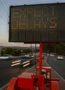 Electronic traffic sign stating Expect Delays with blurred traffic