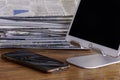 Electronics tablet and cell phone with stand and stack of newspapers on desk in the background. Royalty Free Stock Photo