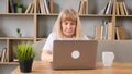 An elederly woman sitting in front of her laptop looking stressed and worried.