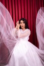 Elegance Asian woman wearing a wedding dress with flying fabric around her in front of the red curtain Royalty Free Stock Photo