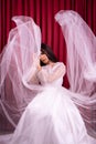 Elegance Asian woman wearing a wedding dress with flying fabric around her in front of the red curtain