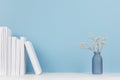 Elegance home decor - white books and small glass vase with dried flowers on soft light white wood table and blue background.