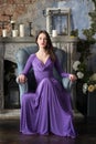 Elegance woman in long violet dress sitting on chair. Indoor