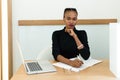 Elegant African or black American woman holding chin working at desk with notepad and laptop in office Royalty Free Stock Photo