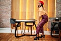 Elegant afro american woman in red french beret, big gold neck chain polka dot blouse and leather pants pose indoor Royalty Free Stock Photo