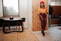 Elegant afro american woman in red french beret, big gold neck chain polka dot blouse and leather pants pose indoor Royalty Free Stock Photo