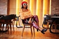 Elegant afro american woman in red french beret, big gold neck chain, sunglasses, polka dot blouse and leather pants pose indoor Royalty Free Stock Photo