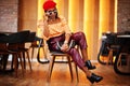 Elegant afro american woman in red french beret, big gold neck chain, sunglasses, polka dot blouse and leather pants pose indoor Royalty Free Stock Photo