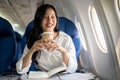 An elegant Asian businesswoman is sipping coffee while looking at the view outside the plane window Royalty Free Stock Photo