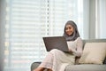 Elegant Asian Muslim woman using laptop to manage her tasks while relaxing on sofa Royalty Free Stock Photo