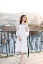 Elegant asian woman in white dress standing on rooftop terrace looking at city background skyline view of old European