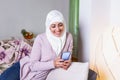 Elegant attractive female muslim using mobile smartphone searching online information when she sitting on sofa couch relaxing.