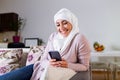 Elegant attractive female muslim using mobile smartphone searching online information when she sitting on sofa couch relaxing.