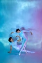 Elegant ballet dancers in white attire performing artistic dance move in neon light against gradient studio background. Royalty Free Stock Photo