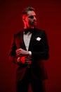 elegant bearded man wearing black tuxedo, looking to side and fixing sleeves Royalty Free Stock Photo