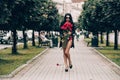 Elegant beautiful brunette woman in red shorts and black coat posing in the alley with a big bouquet of red roses Royalty Free Stock Photo