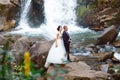 Elegant beautiful wedding couple posing near beautiful grand waterfall in mountain. luxurious wedding dress. Marriage couple outdo Royalty Free Stock Photo