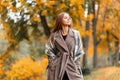 Elegant beautiful young woman in a fashionable long coat with a stylish knitted scarf stands in the park and enjoys the autumn Royalty Free Stock Photo