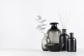 Elegant blank black bottles, glass vase for home decor on soft light white wood table with silver leaves as template.
