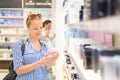 Elegant blond young woman choosing perfume in retail store.