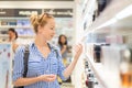 Elegant blond young woman choosing perfume in retail store.