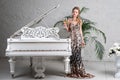 Elegant blonde lady with glass of wine in restaurant standing near white grand piano in a luxury classic interior. Beautiful sexy Royalty Free Stock Photo