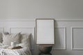 Elegant boho bedroom interior. Vertical wooden picture frame mockup on modern organic shaped side table. Cup of coffee