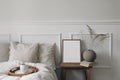 Elegant boho bedroom interior. Vertical wooden picture frame mockup on old bedside table. Cup of coffee. Ball vase with