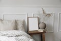 Elegant boho bedroom interior. Vertical wooden picture frame mockup, vintage bedside table. Ball vase with dry grass on