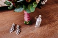 Elegant bridal earrings and perfume on the wooden floor next to the wedding bouquet