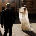 elegant bride holding veil and posing with groom in sunlight under flying birds in old courtyard in european street. luxury