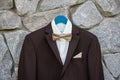 Elegant brown male tuxedo with white shirt and bow tie hanging on stone wall outdoors, copy space. Modern men accessories. Royalty Free Stock Photo